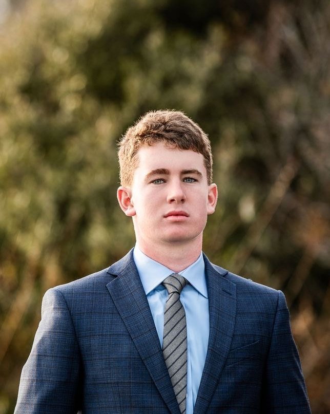 Alister Jackson in a navy suit, light blue shirt and gray striped tie, outdoors